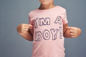 A close-up of a young boy proudly pointing to his pink custom t-shirt reading "I'M A BOY!", showcasing the fun, high-quality results of Boy's Affordable T-Shirt Printing for parents seeking cheap t shirts printing and durable affordable custom t shirts.