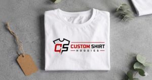 A cleanly folded white t-shirt featuring a red and black custom logo resting on a textured grey surface beside a blank cardboard tag, representing the premium retail-quality output of Custom T-Shirts Little Rock, Arkansas for all your custom apparel and t shirt custom printing needs.
