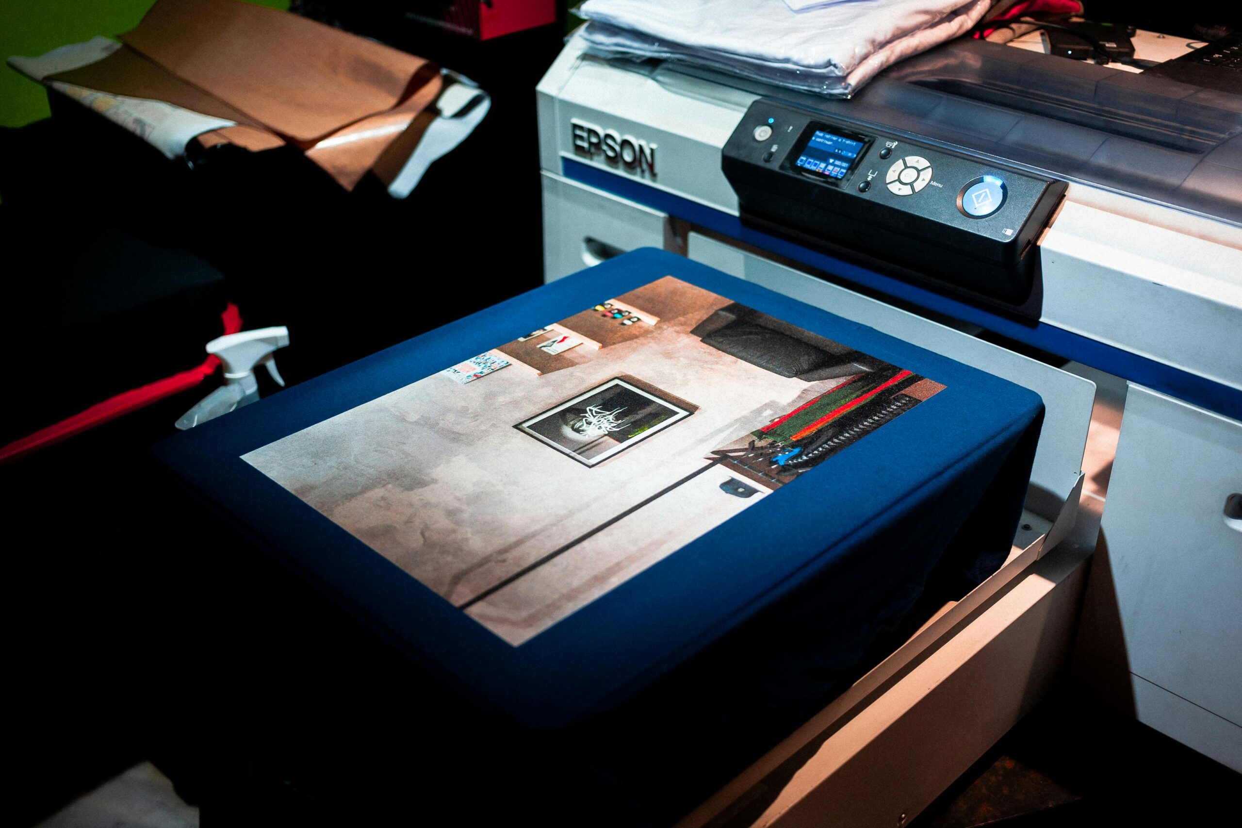 A close-up view of a high-quality photograph being printed directly onto a dark blue garment using a professional commercial printer, showcasing the precise and detailed craftsmanship involved in creating custom Memorial T-Shirts in Little Rock for families seeking respectful Memorial T-Shirts Little Rock services and beautiful memorial shirts.